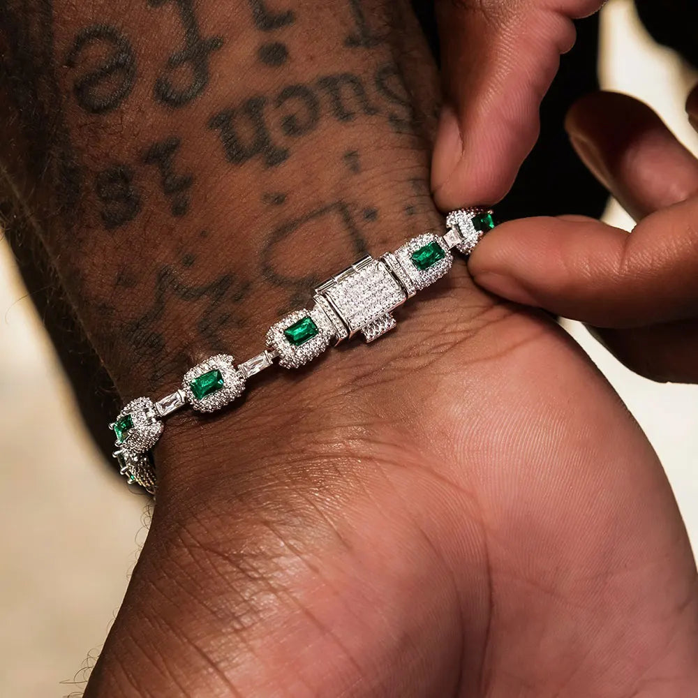 Person wearing a diamond and emerald bracelet on a tattooed arm